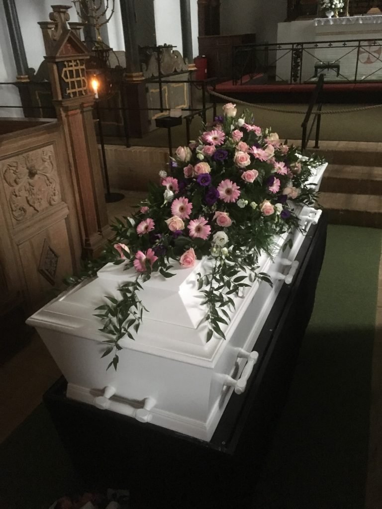 Hvid kiste med lyserød blomsterdekoration i kirke